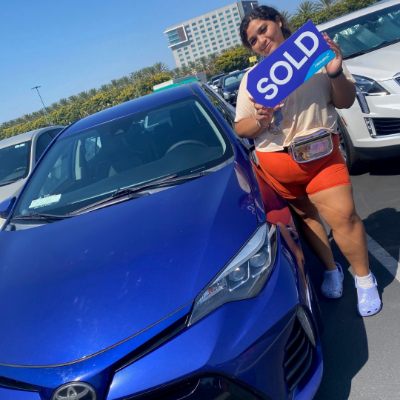 Woman holding a SOLD sign next to her new vehicle