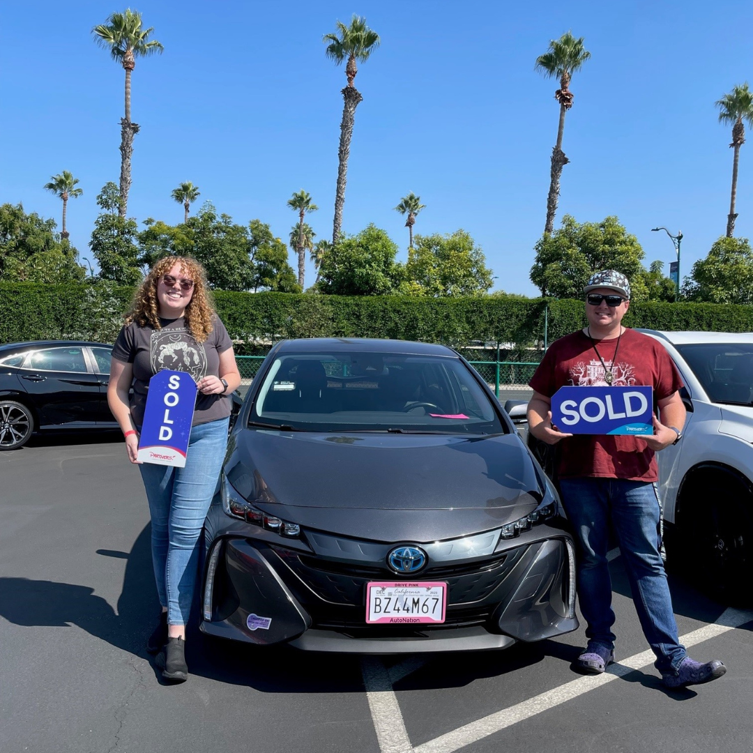 Couple holding a Sold sign next to their new vehicle