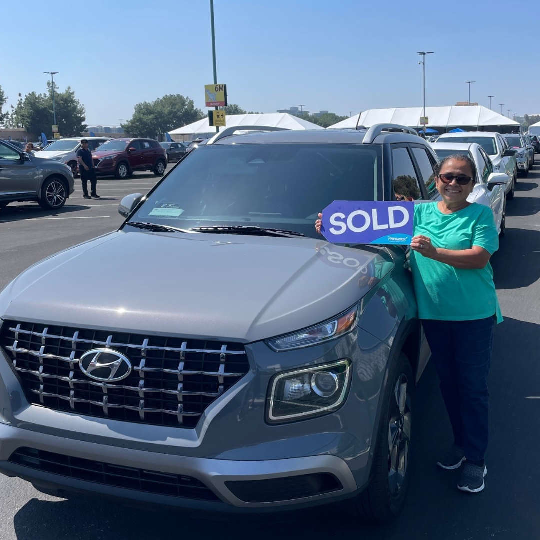 Lady holding a sold sign next to her vehicle